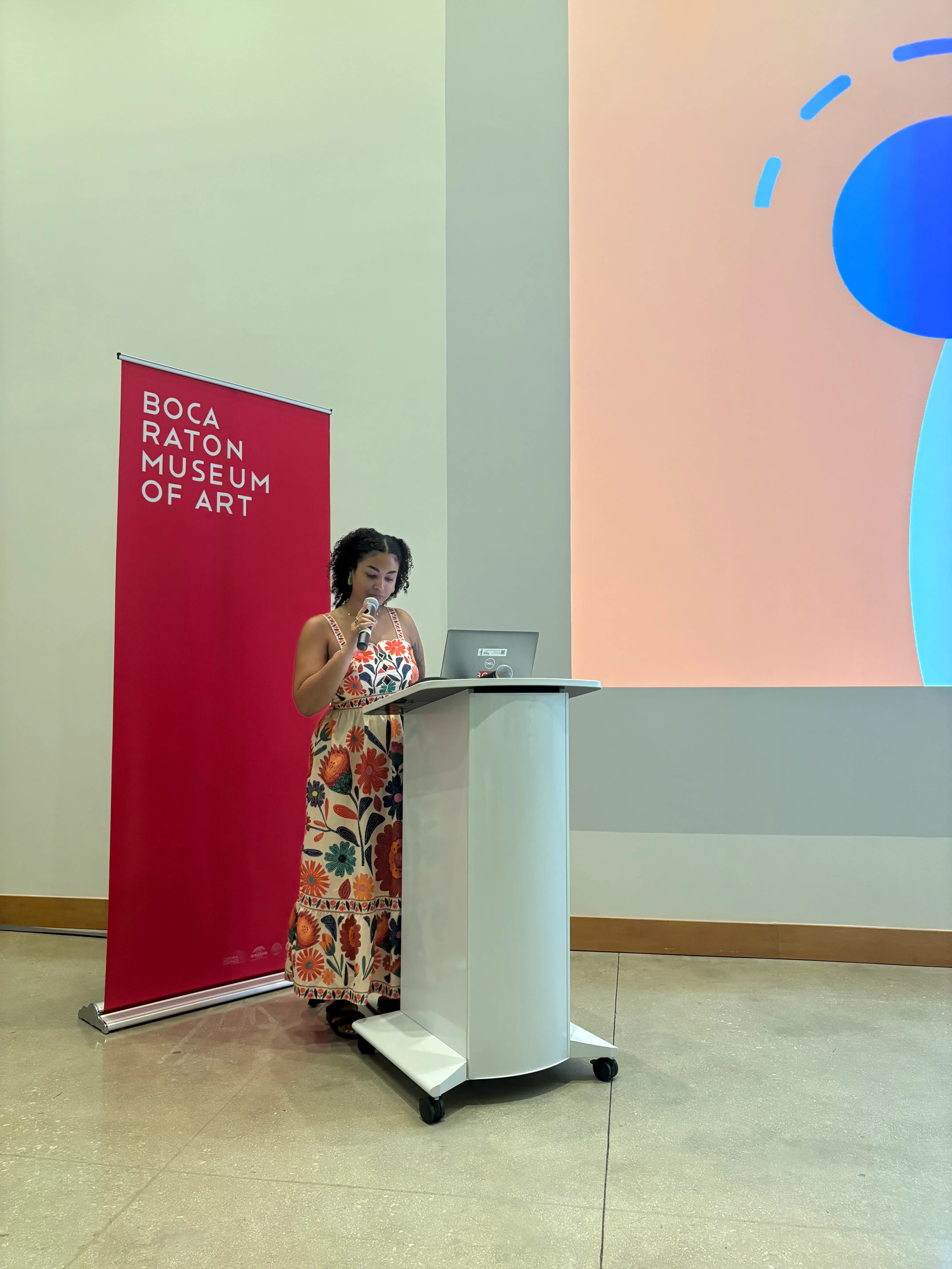 Areshika speaking at a podium beside a Boca Raton Museum of Art banner