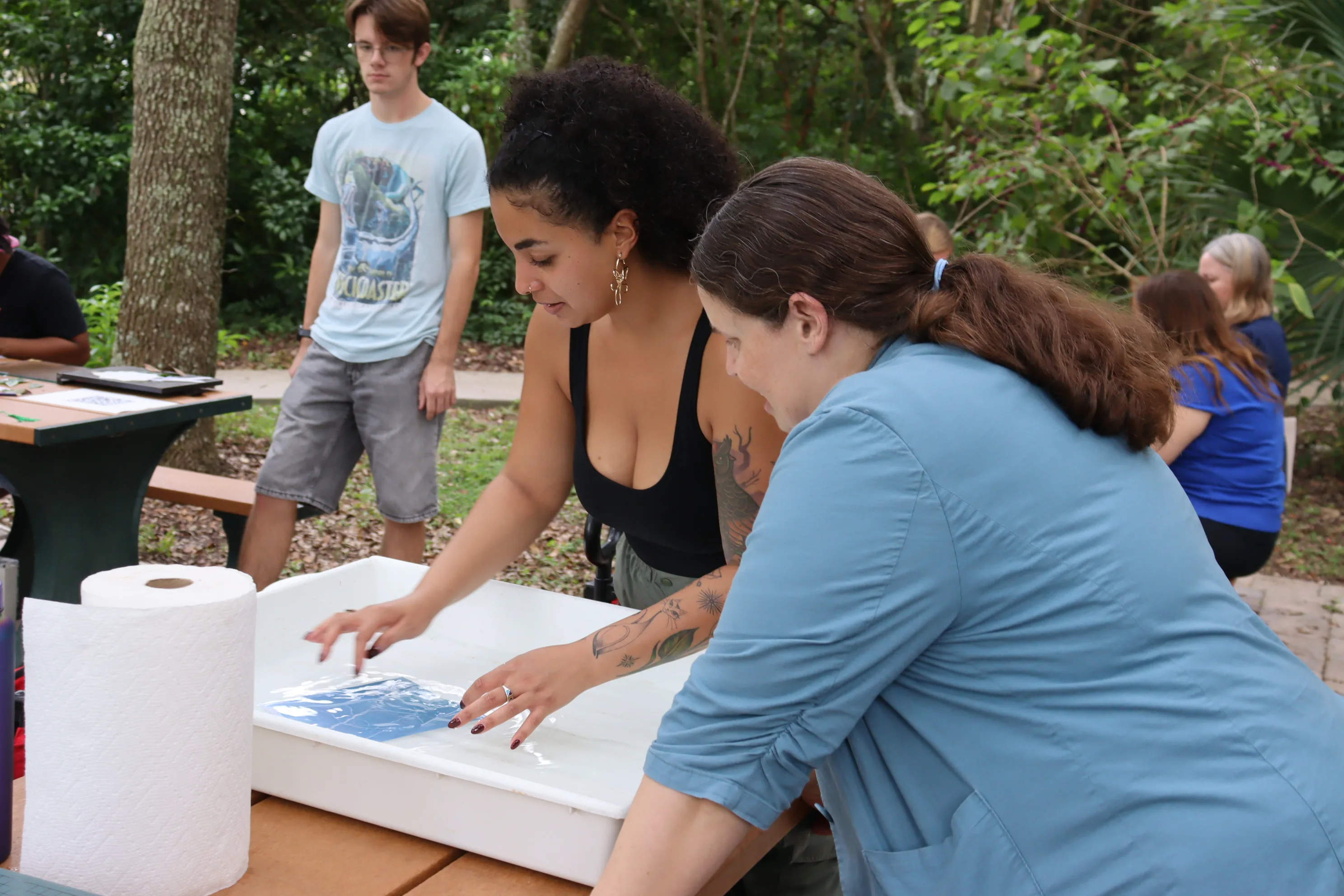 Participants placing a cyanotype print into a water tray at an outdoor workshop