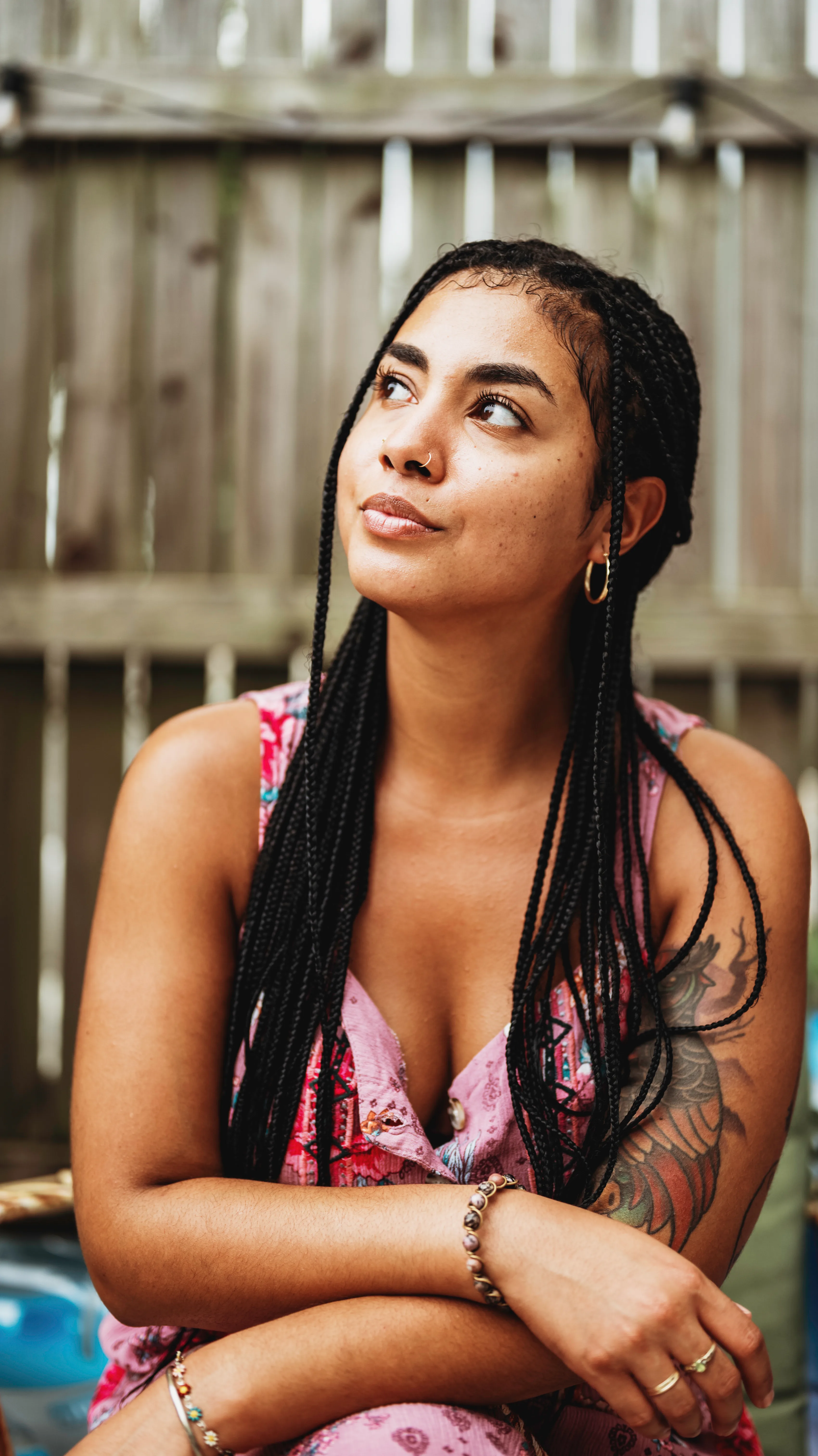 Areshika with long braids gazing upward in front of a wooden fence