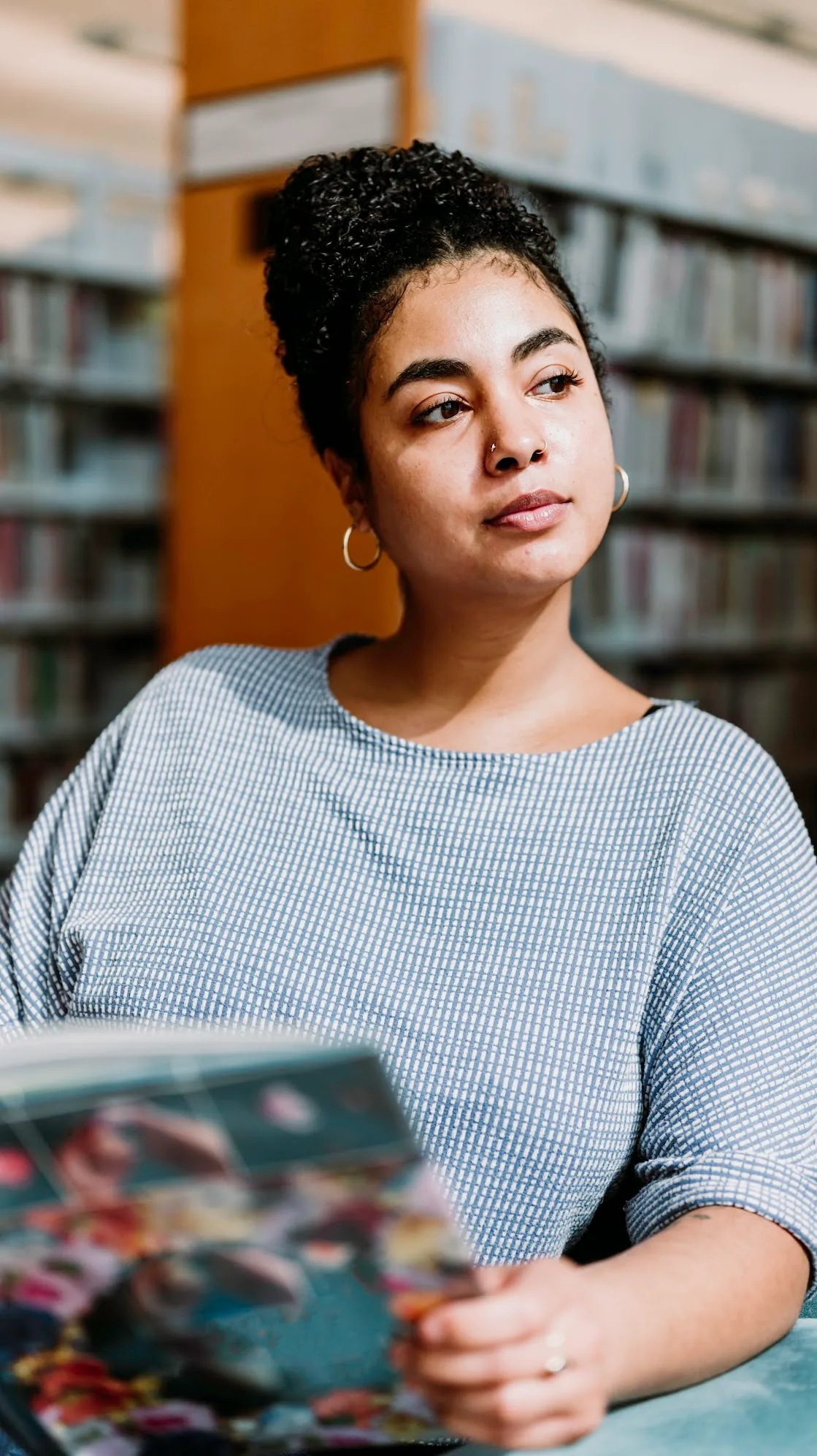 Areshika seated in a library holding a book, looking to the side
