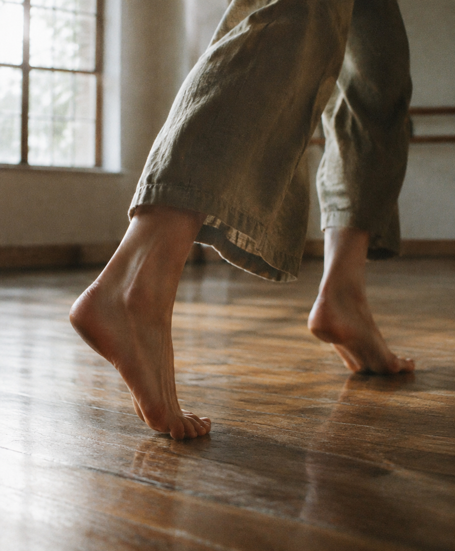Dancer's bare feet mid-step on a wooden studio floor